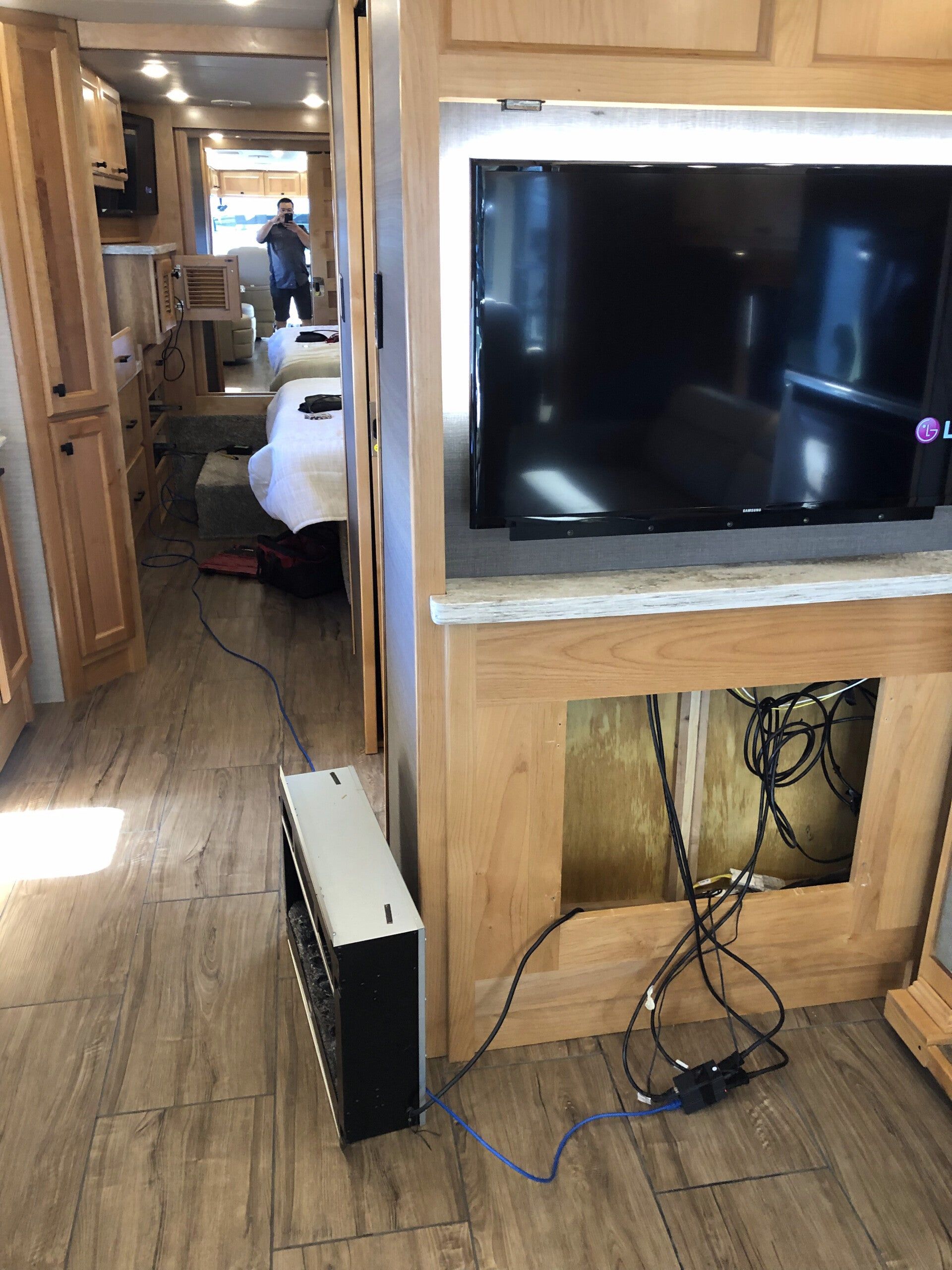 RV interior with wall-mounted TV, visible cables, and a hallway leading to a person in the back.