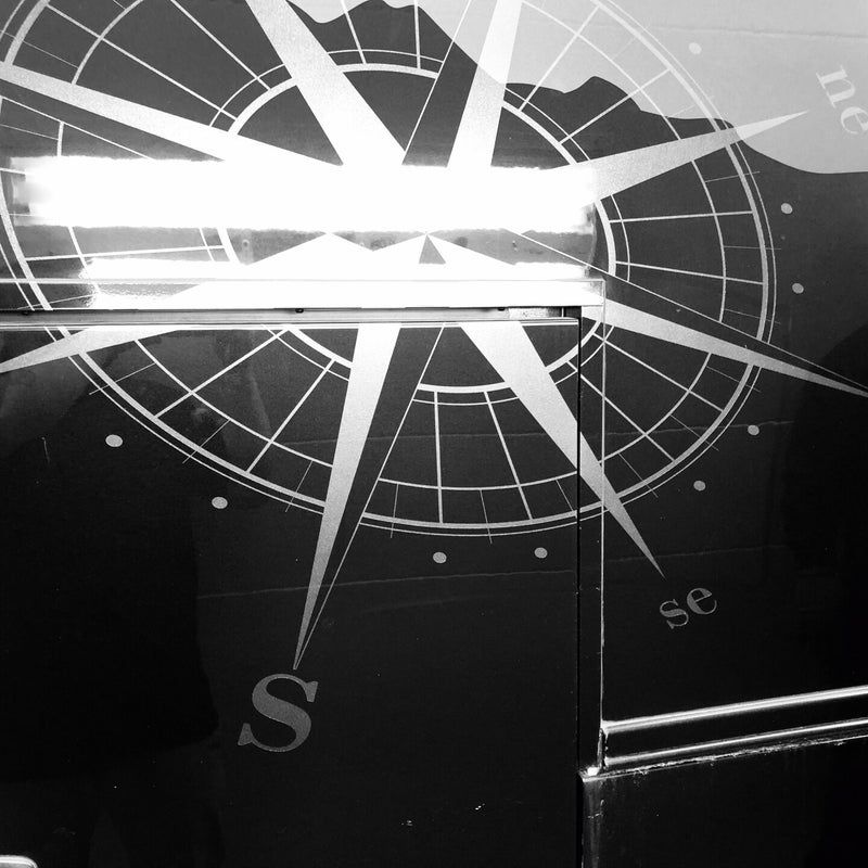 Black-and-white compass rose graphic with bright light flare and directional letters on a dark surface