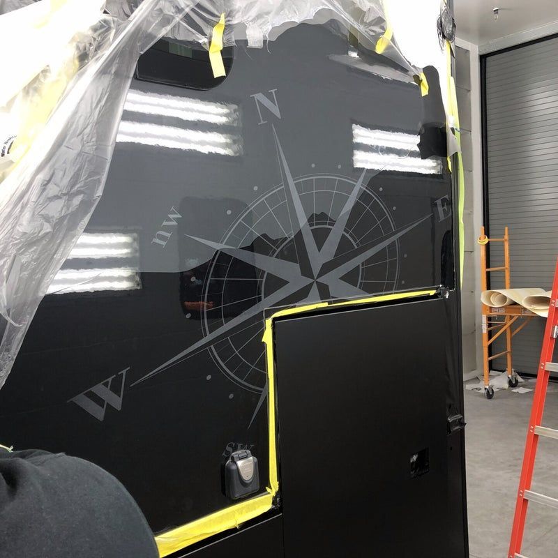 Black glossy panel being installed, taped off in a workshop with a ladder nearby.