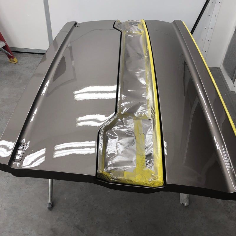 Car roof panel being repaired, with silver filler and yellow masking tape along the center seam.