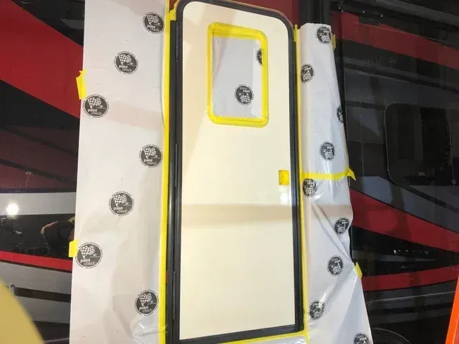 White RV door with yellow trim and black border, surrounded by silver rivets on a red-and-black vehicle exterior