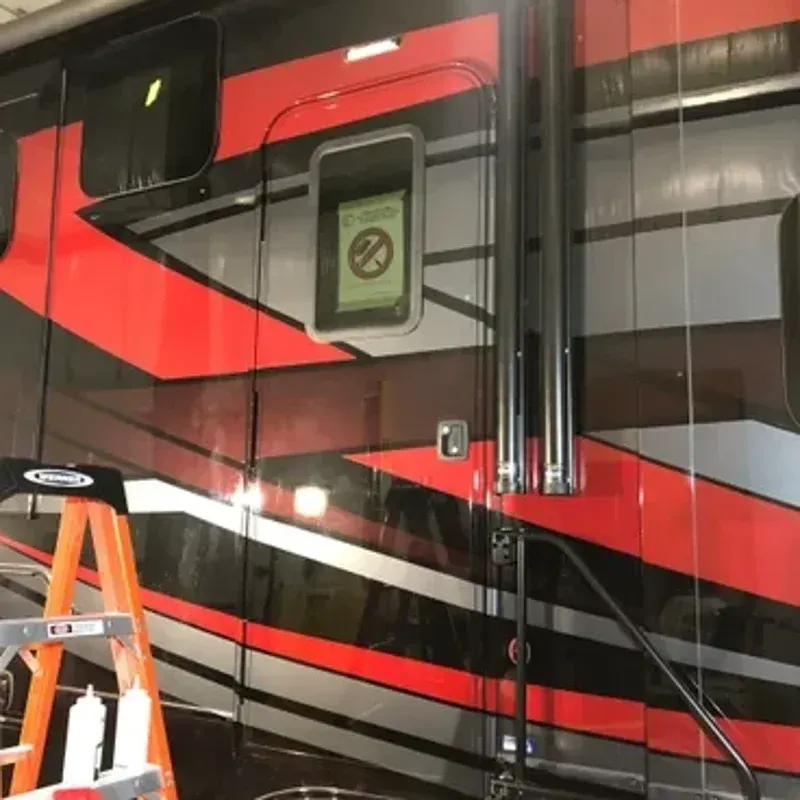 Red and black RV side with door, window, and orange ladder in garage