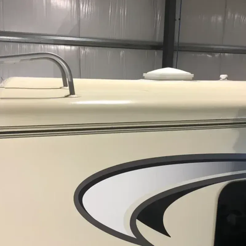 Beige RV side with chrome handrail and black-and-white swirl decal in a metal garage