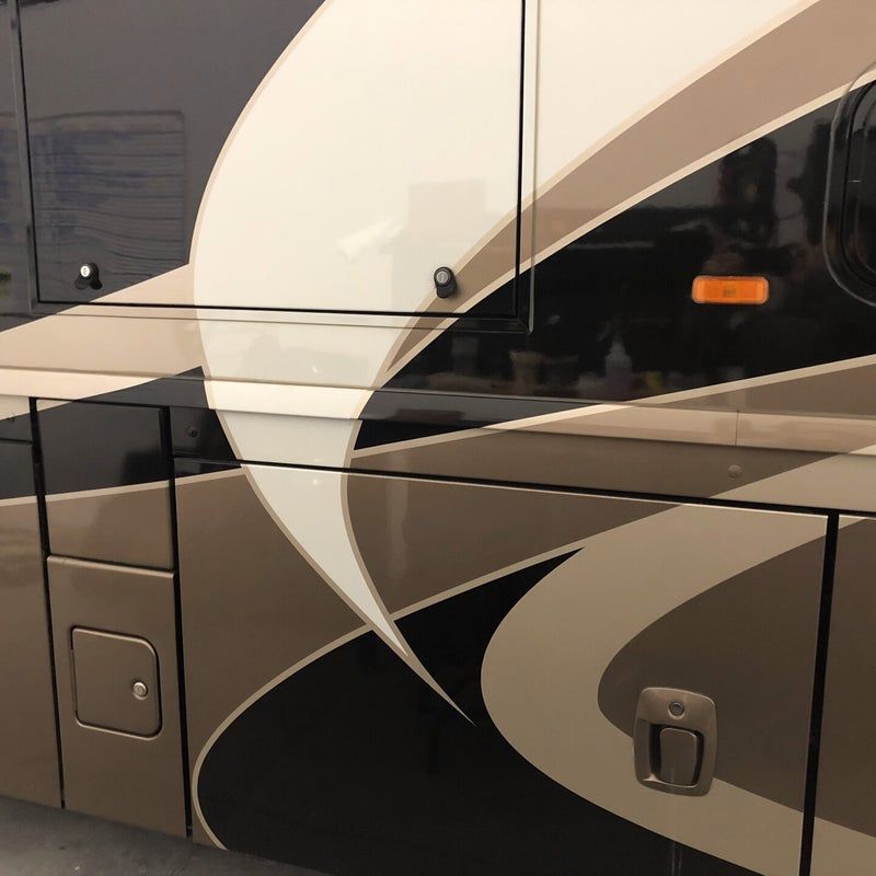 Side of a beige-and-black RV with sweeping gray graphics and storage compartment doors