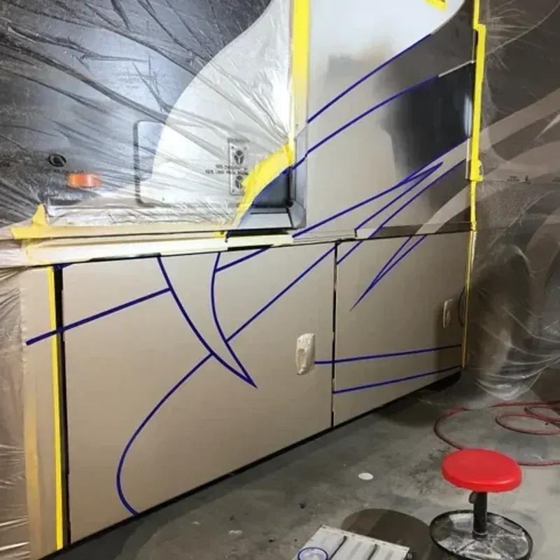 Interior wall with beige panels outlined in blue tape, a plastic-covered window, and a red stool on the floor