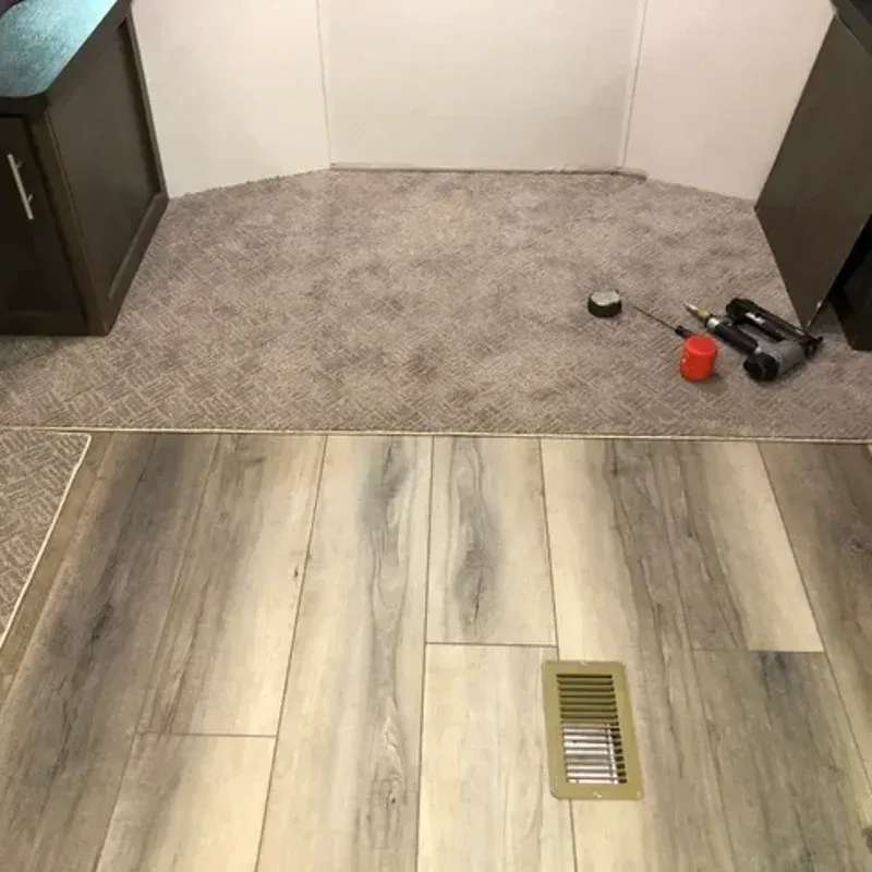 Carpeted room with a wood-look floor and vent; a few tools and a red item sit in the corner.