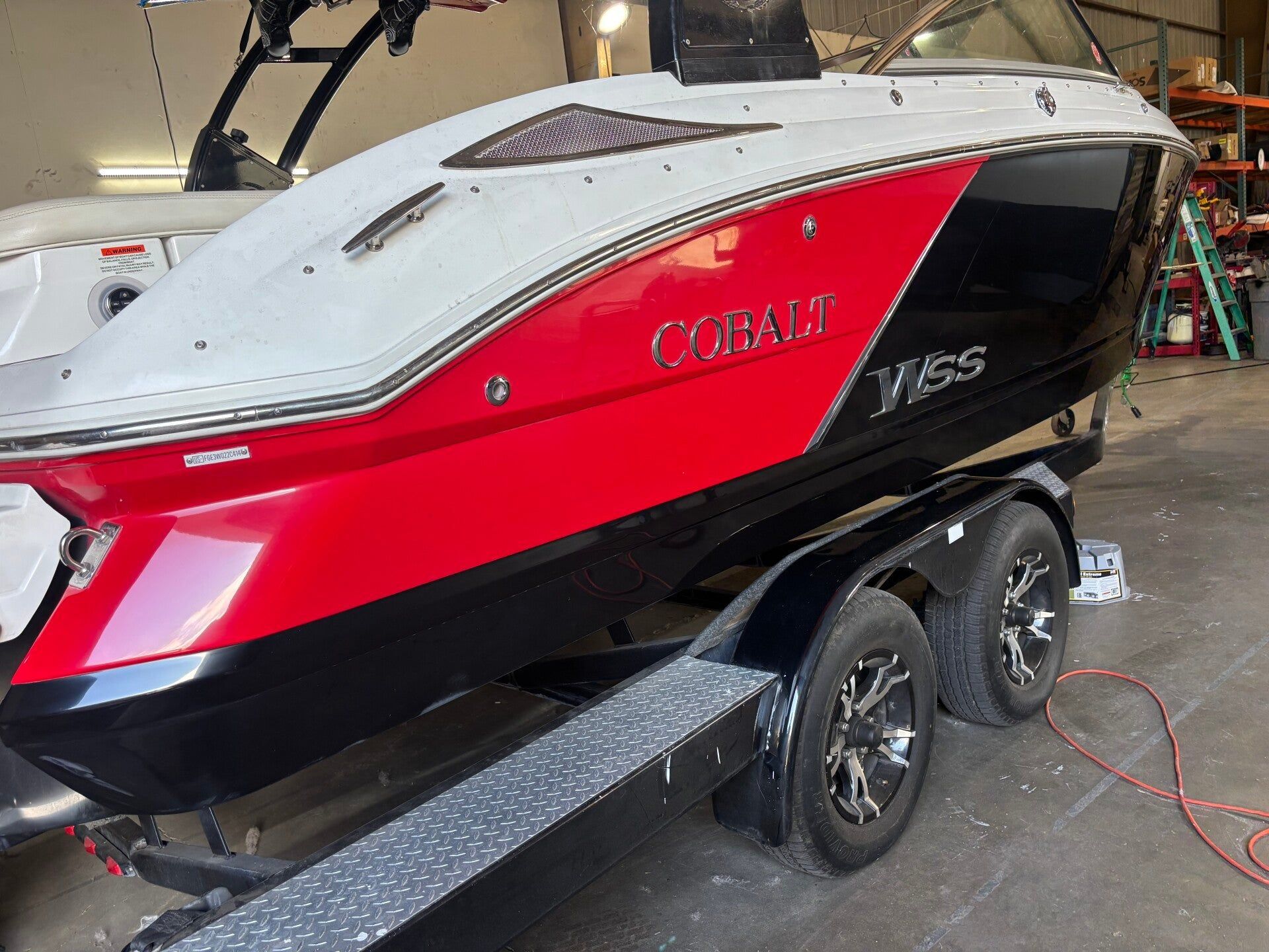 Red and black boat on a trailer in a garage, with a gray top and dual axles.