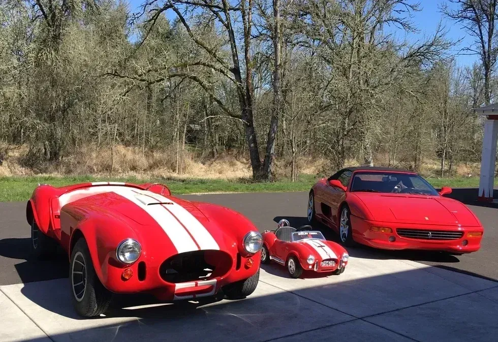 Three red sports cars parked outdoors, including a large striped race car and a small toy car.