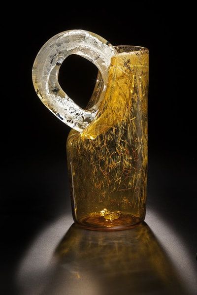 Amber glass vase with a circular handle, set against a black backdrop, reflecting light.