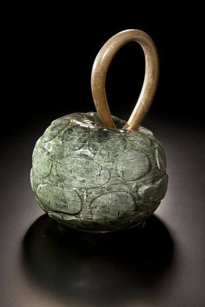 Green, textured, spherical object with a golden loop handle against a black backdrop.