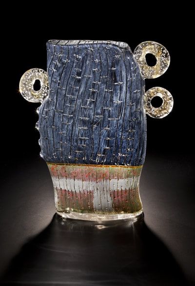 Glass sculpture of a head with blue and white textured body, red/white/green base, and three round gold-colored rings.