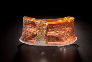Copper and resin micro-coil, showing layers and a clear central void, set against a black background.