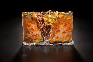 Abstract glass sculpture; orange spotted with yellow and brown accents against black.