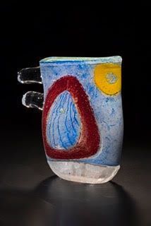 Colorful glass mug with abstract shapes: red triangle, yellow circle, blue background.