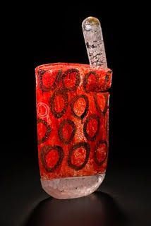 Ancient glass cup, red with brown circles, clear straw, against black backdrop.