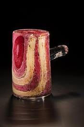 Glass mug with red and cream swirl design, clear handle, on reflective surface.