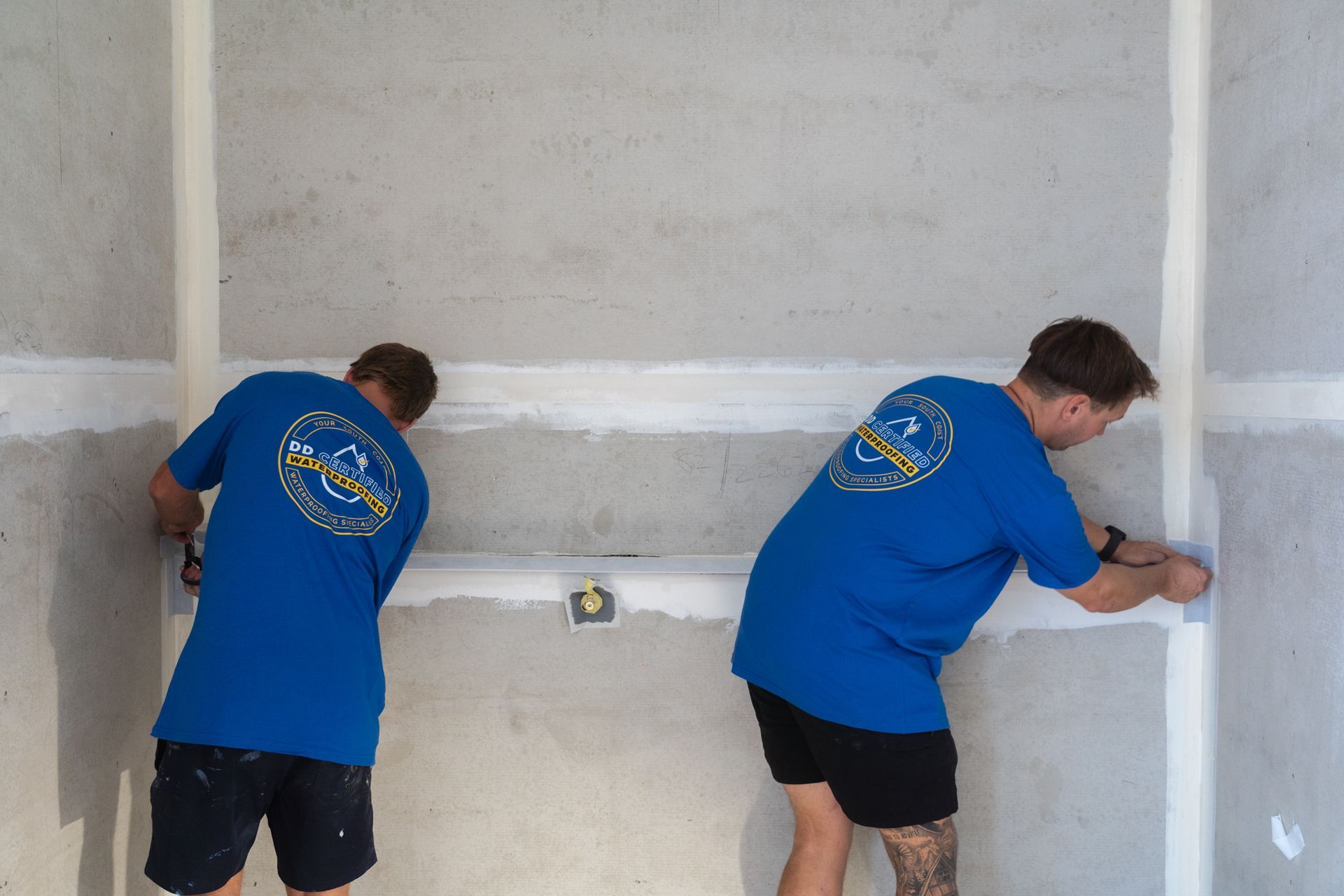 Two men in blue shirts are working on a wall