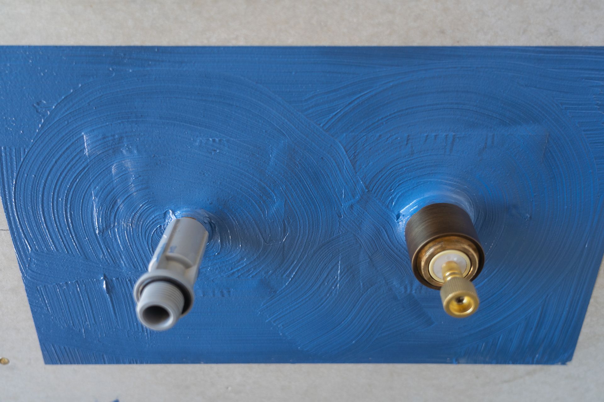 Two faucets are sitting on a blue surface.
