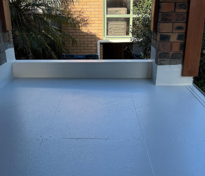 A balcony with a white floor and a brick building in the background.