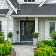 Front entry of a gray house with dark door, white siding, potted plants, and a curved stone walkway