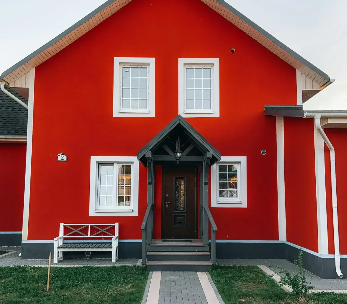 Bright Red House With White Trim, Dark Front Door, And a Paved Walkway Leading to The Entrance.