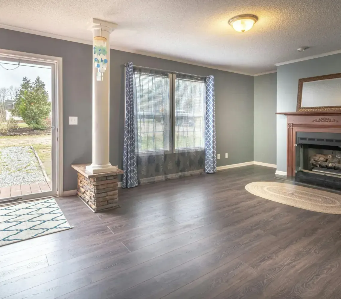 Empty Living Room With Dark Floors, Gray Walls, Fireplace, And Open Door to Outside
