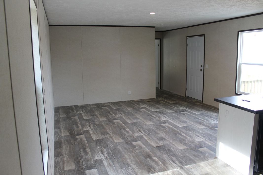 An empty living room in a mobile home with a wooden floor.