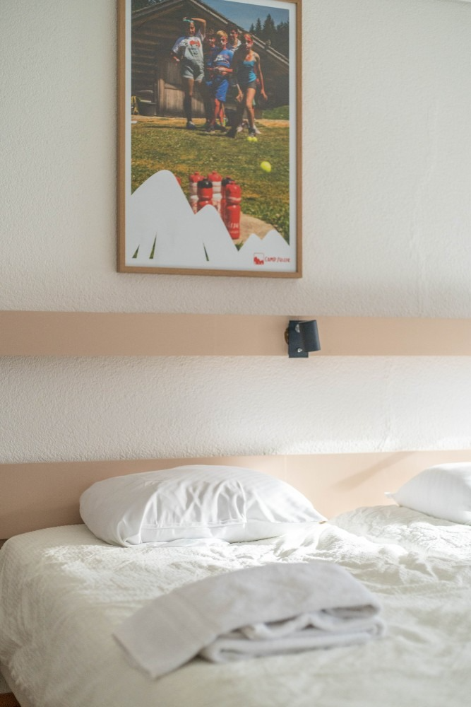 Bed with white linens, folded towel. Poster of people outdoors on wall.