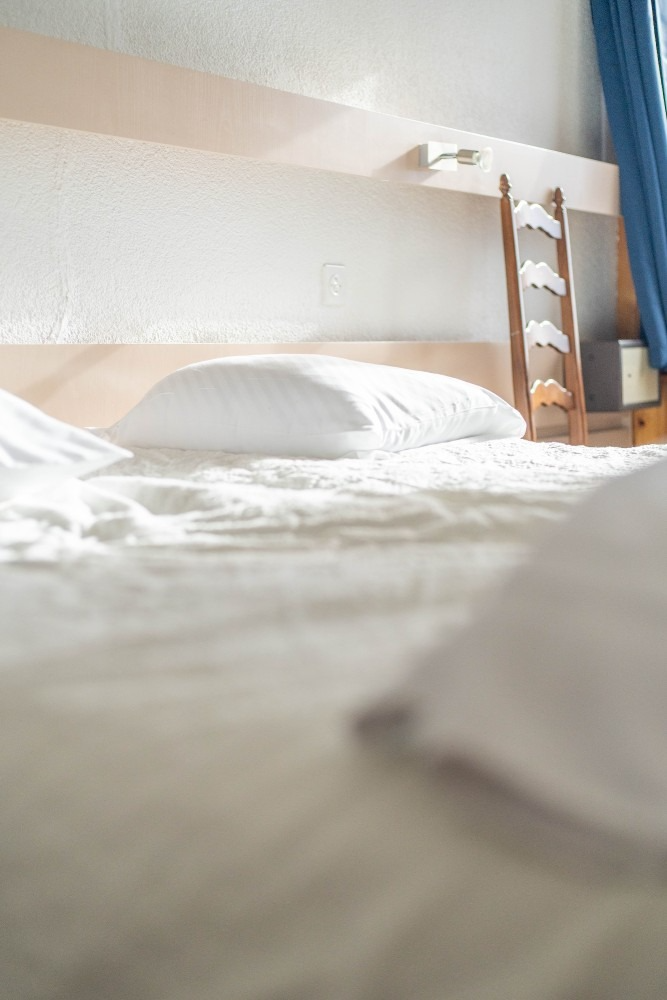 White bed with pillows, small wooden ladder, and a blue curtain.