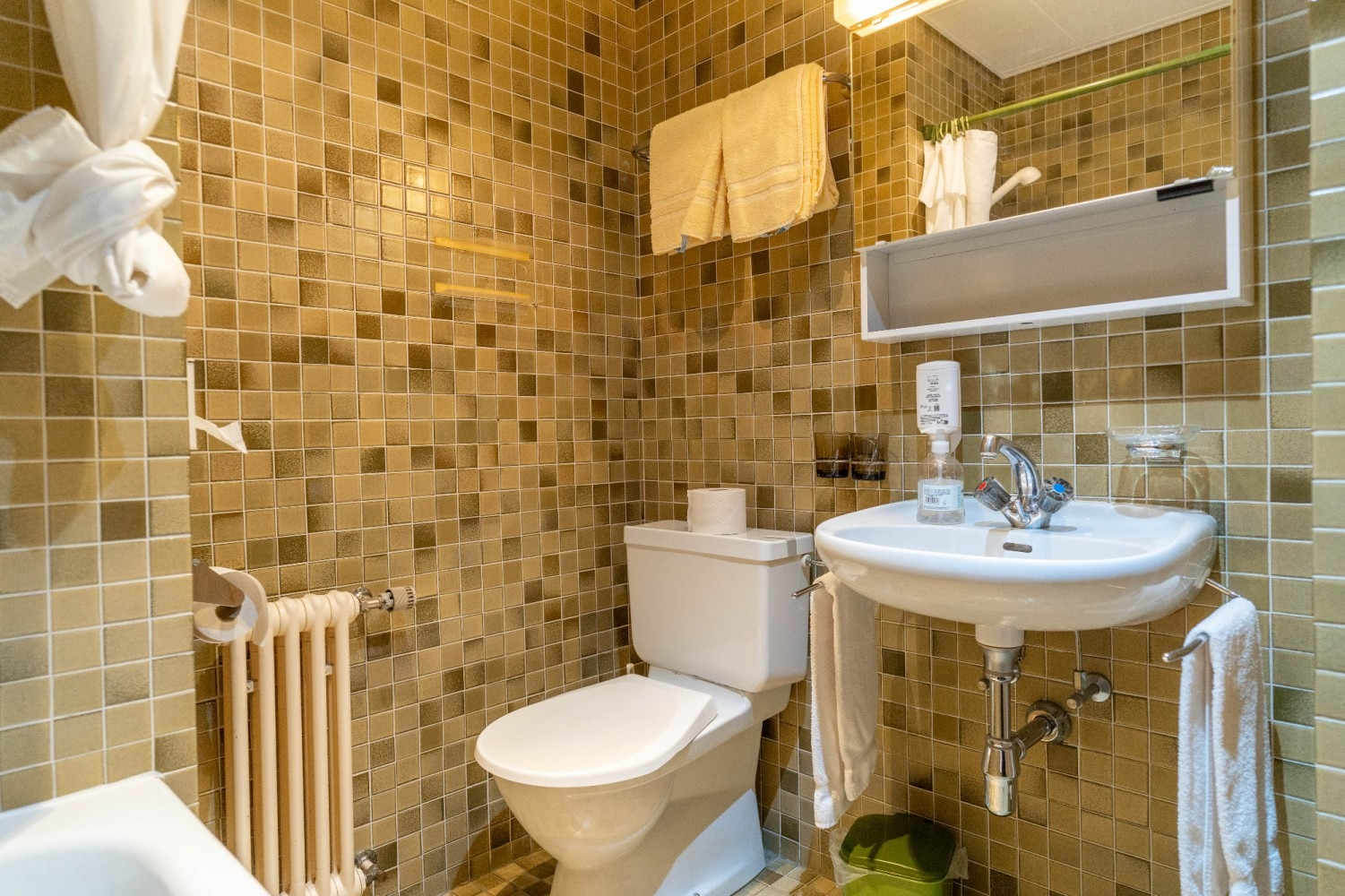 Small bathroom with brown tile walls, white toilet and sink. Towels hang on a rack.