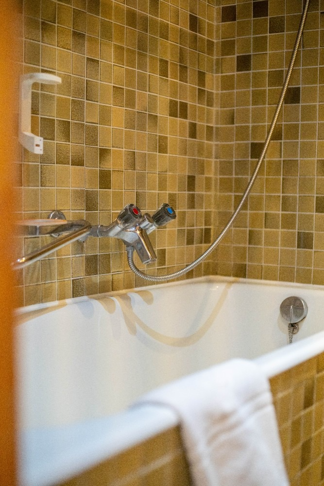 Bathtub with chrome fixtures, tan tile wall, and a white towel on the edge.