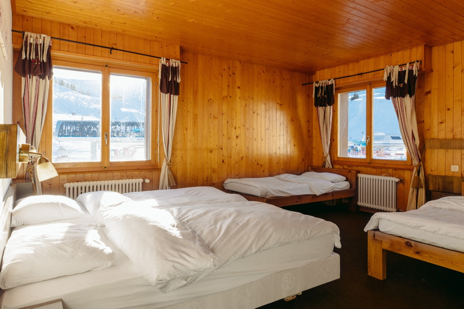 Bedroom with three beds, wood-paneled walls, and large windows overlooking a snowy landscape.