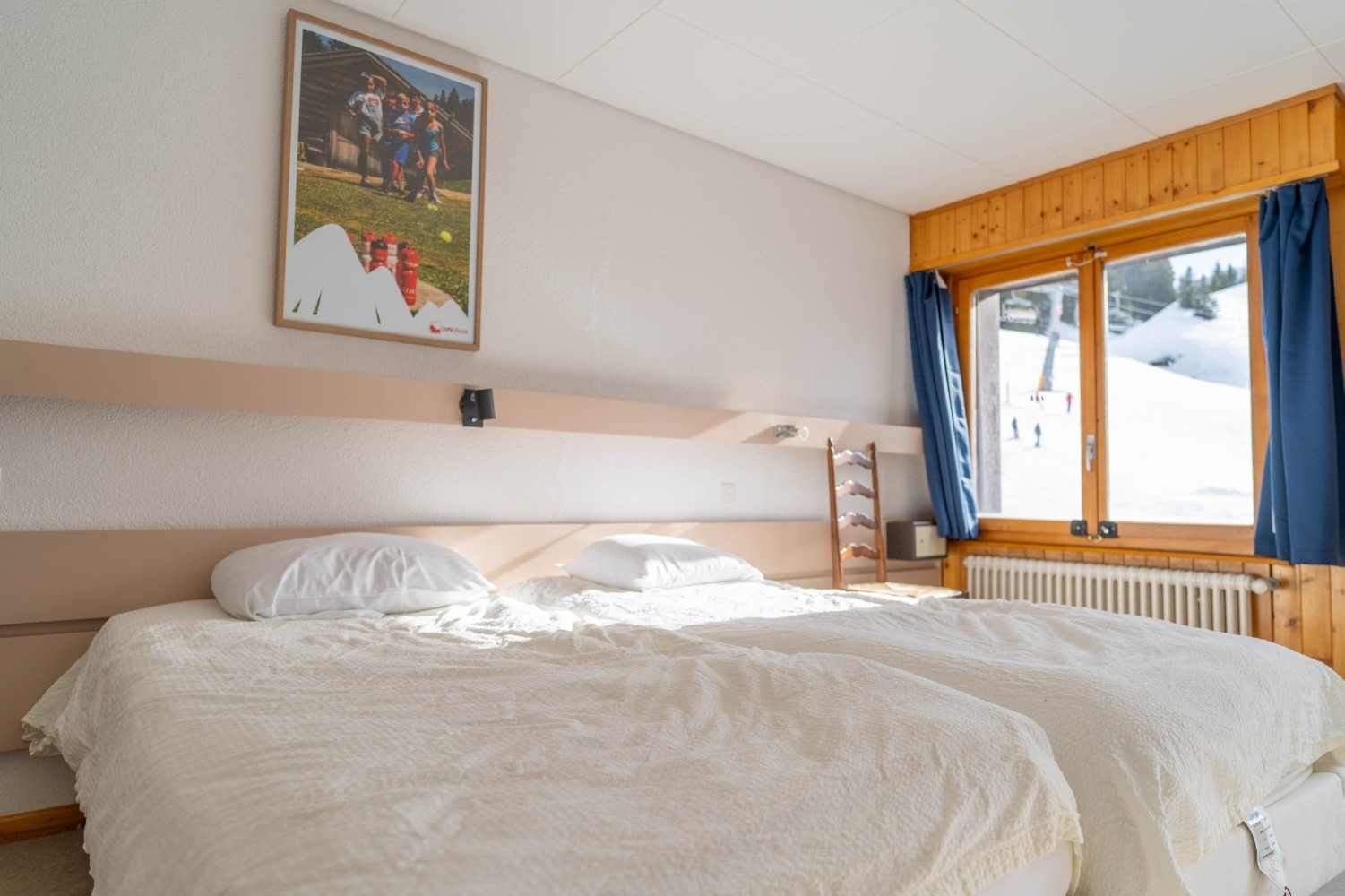 Bedroom with two beds, a window overlooking a snowy landscape, and a framed poster on the wall.