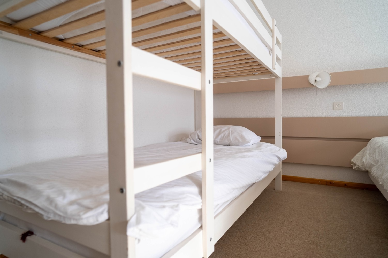 White bunk beds in a room with white walls and beige carpet.