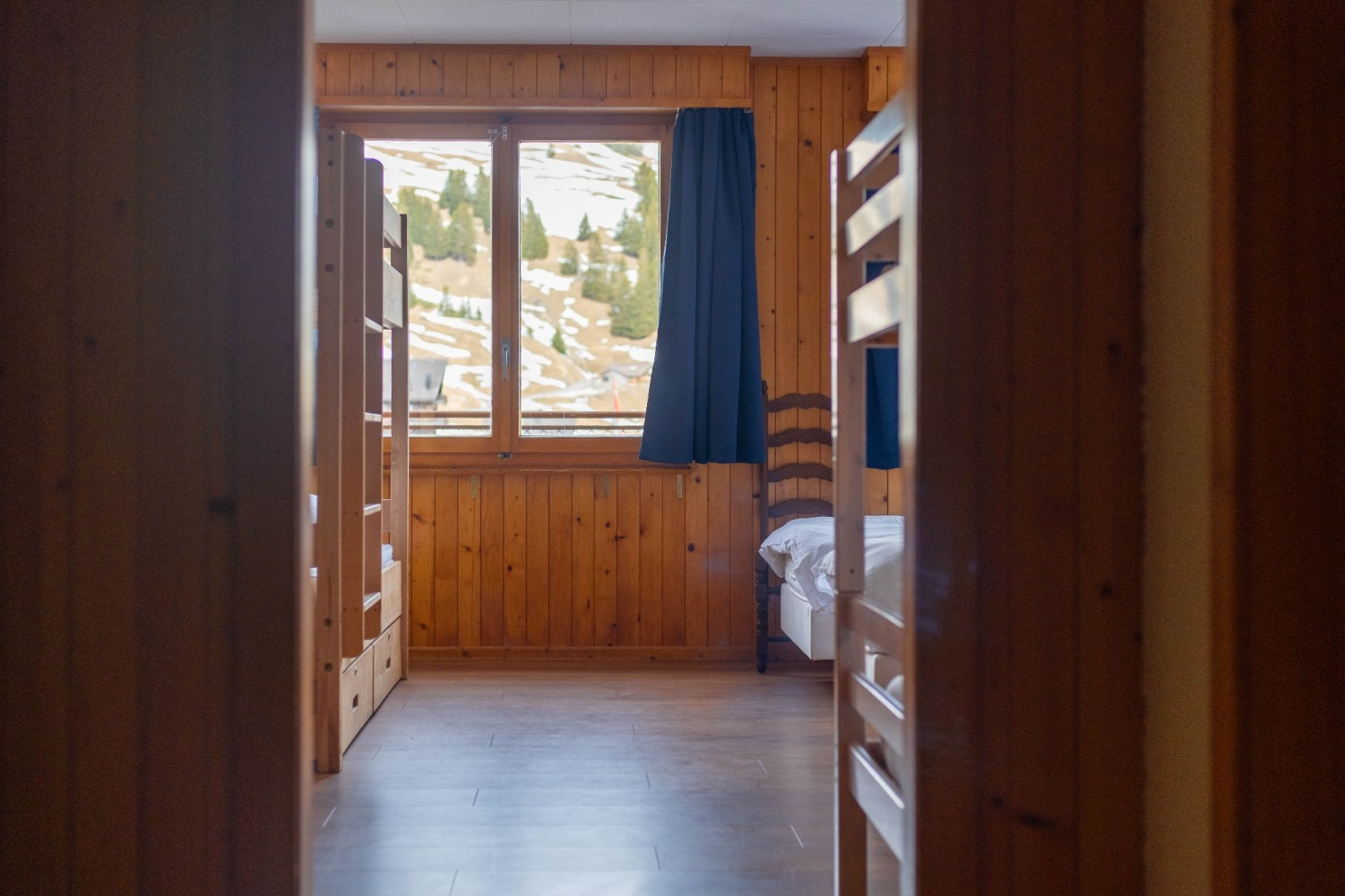 Wooden room interior with bunk beds and a window with mountain view.