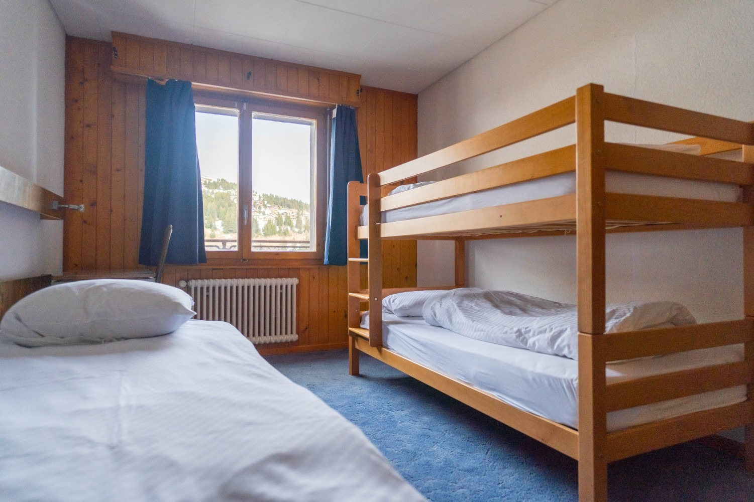 A small bedroom with bunk beds, a single bed, and a window with dark curtains.