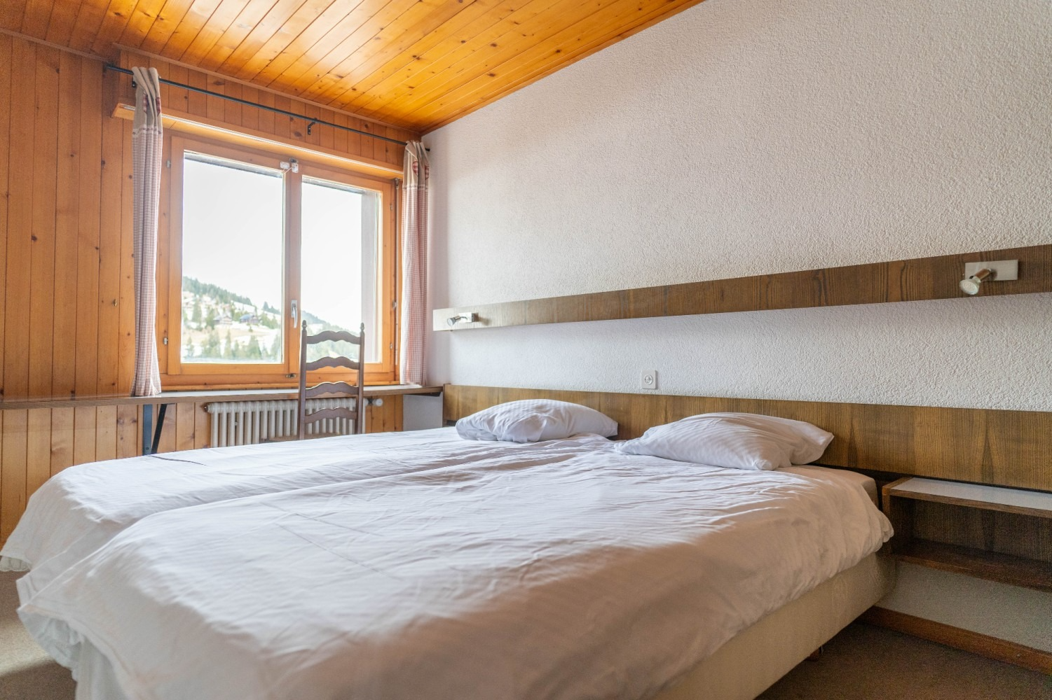 Bedroom with two twin beds, window overlooking mountain scenery, wood paneling, and white bedding.