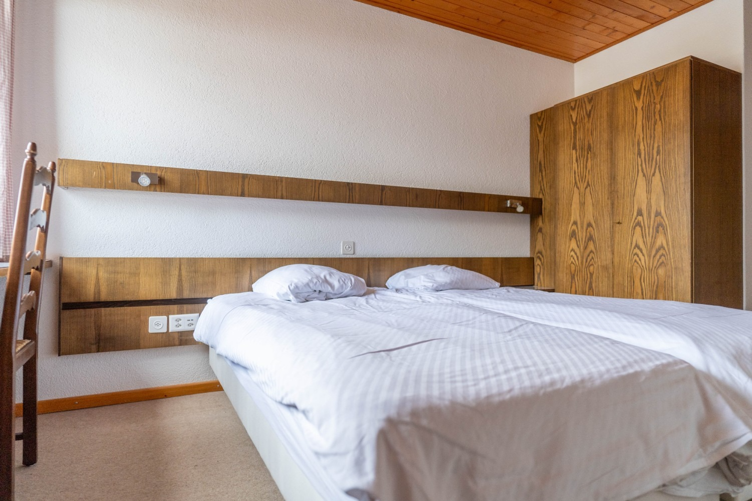 Bedroom with white bedding, wooden headboard, and a wardrobe.