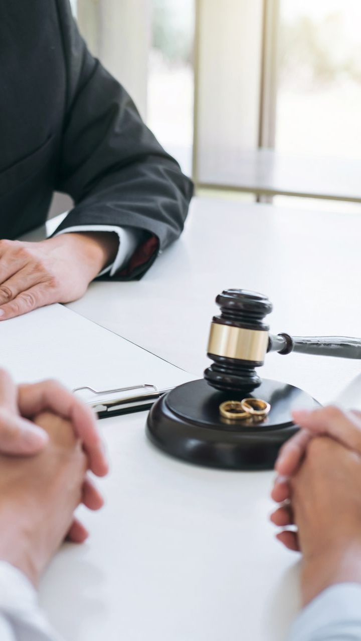 two people's hands folded in front of a gavel with two wedding bands resting on it