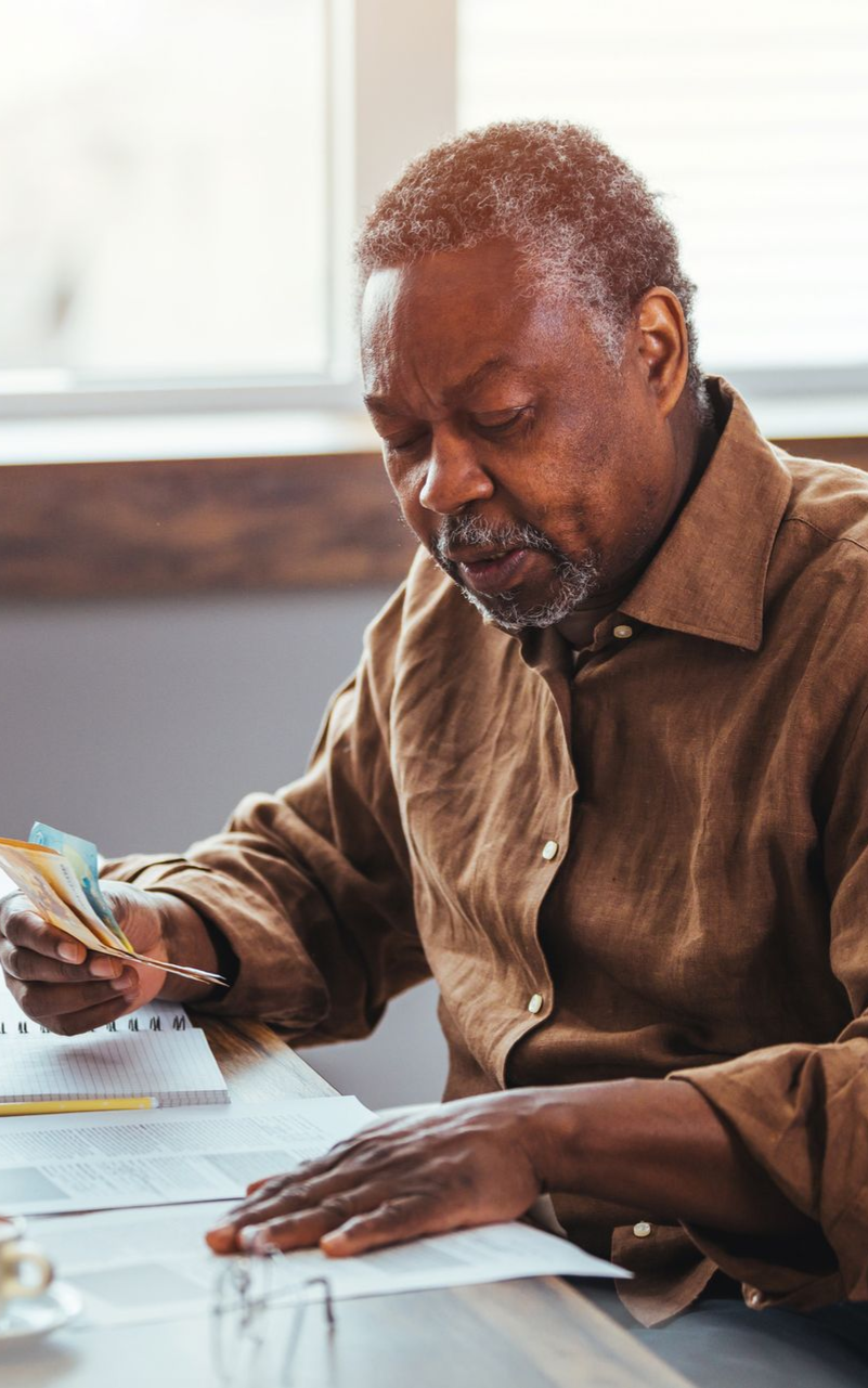 an older man sitting at a desk looking at documents and holding cash