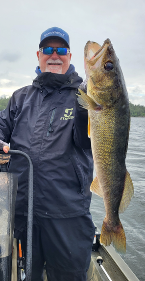 Person on a boat holding a large fish against a cloudy lakeside backdrop.