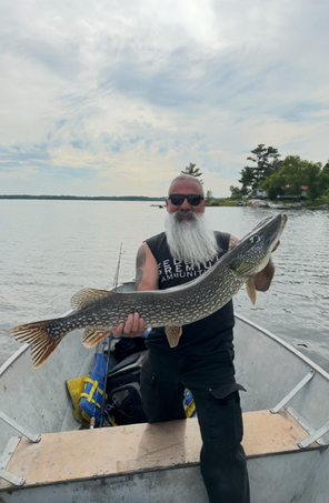 Man holding a large fish on a boat on a calm lake under a cloudy sky