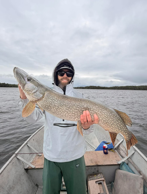 Person holding a large fish on a boat under an overcast sky.