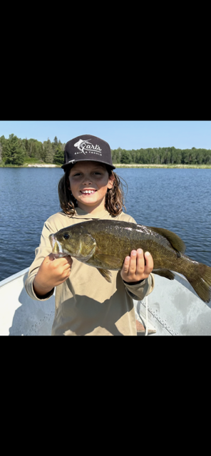 Person holding a large fish by a lake on a sunny day