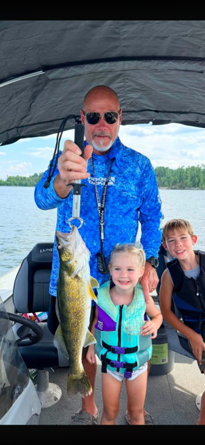 Man holding a large fish with two smiling children on a boat under a canopy.