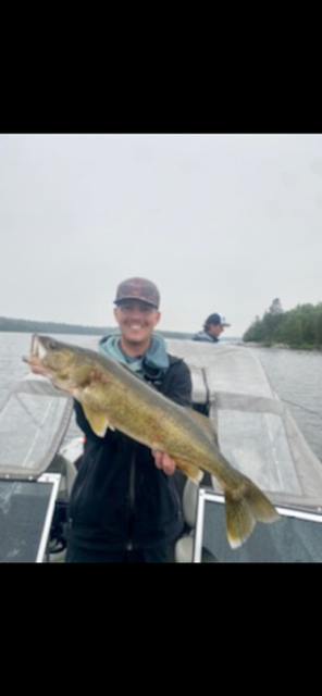 Person on a boat holding a large fish on a cloudy day.