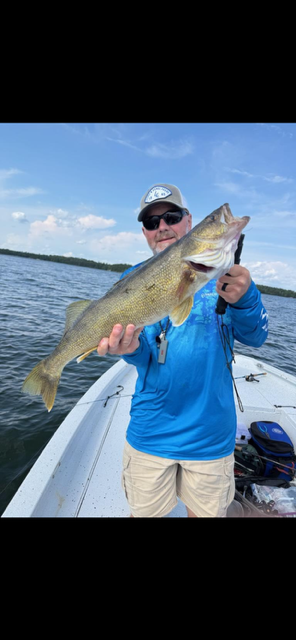 Angler on a boat holding a large bass on a sunny lake.