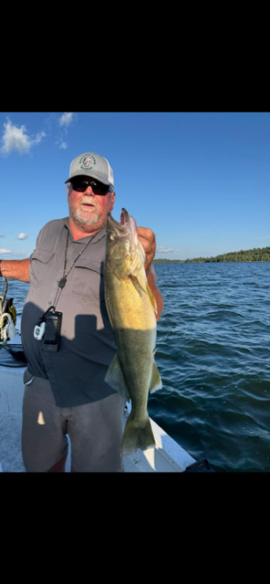 Person on a boat holds up a yellow-green fish on a sunny lake with blue sky.