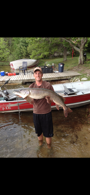 Person holding a large fish beside a red-and-white boat at a muddy riverbank.