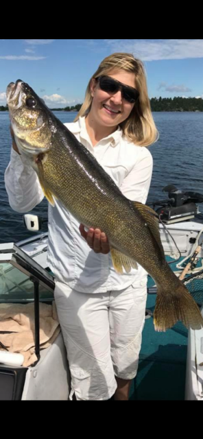 Woman holding a large fish on a boat with water and shoreline in the background